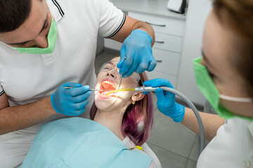male dentist treats a patient's teeth and a female assistant helps him.