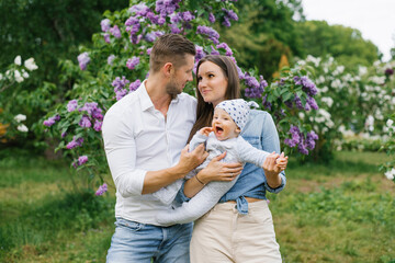 Portrait of a Caucasian family enjoying happy love, father and mother holding a cute little son in their arms, smiling, playing and having fun at home in a summer park