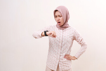 Shocked angry young asian muslim woman standing while looking at wristwatch. Isolated on white