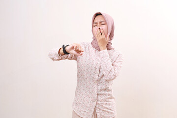 Young asian muslim woman yawning while looking at her wrist watch. Sleepy in ramadan concept