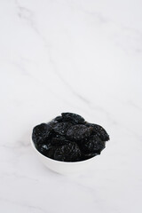 Prunes in a white bowl on a marble table