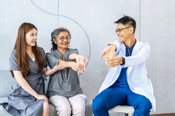 Male doctor teaching physical therapy to Asian senior adult patient and daughter in hospital or...