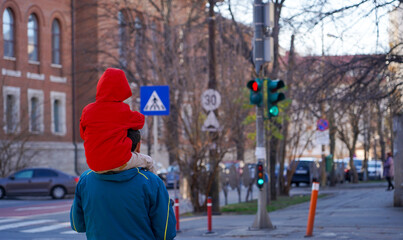 father holding his child on his shoulders at the pedestrian crossing.