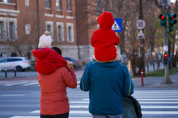 family with two children held on their shoulders waiting for a pedestrian crossing, the green color of the traffic light.