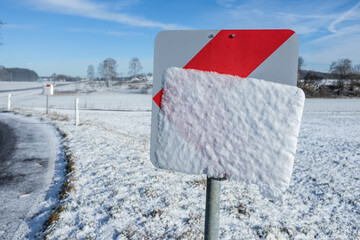Verschneites Verkehrsschild Achtung Kurve an Straße bei Oberstetten/Hohenstein vor blauem Himmel mit Wolken