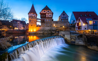 Panoramic view of historic buidings, castle and cascade of Eyach river in old town in Balningen (Baden-Wuerttemberg, Germany). Half timbered and illuminated facades at evening twilight in winter. - obrazy, fototapety, plakaty