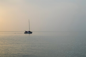 Fishing boat with fishing men floating in sea at sunset time. Calm water surface in evening. Water...