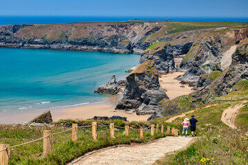 Bedruthan Steps, Cornwall, UK - The famous sea stacks, with pathway and couple in hats looking at view. - obrazy, fototapety, plakaty