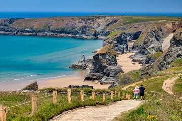Fotobehang Bedruthan Steps, Cornwall, UK - The famous sea stacks, with pathway and couple in hats looking at view. © Colin & Linda McKie