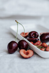 whole cherries and halves with cherry pits in a white rectangular plate on a white tablecloth, next to the plate there are a couple of cherries