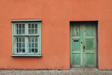 A vintage red house with old green door and window. Ancient wooden door in old building wall.