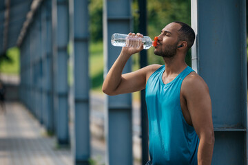Well-built handsome sportsman drinking water after workout