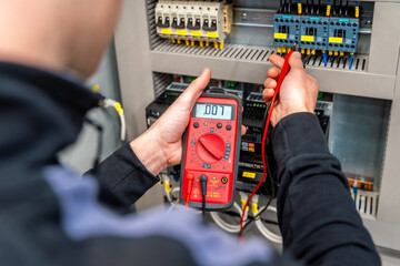 Worker measuring and repairing an electrical system panel - obrazy, fototapety, plakaty