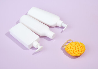 White dispensers with personal care products and a yellow, brightly colored shower sponge on a purple background. Skincare and beauty routine.