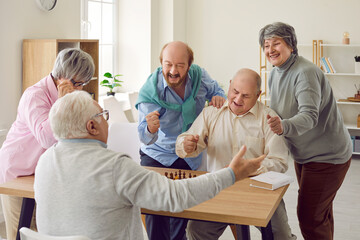 Group of happy overjoyed senior people playing chess in nursing home sitting at the table. Retired...
