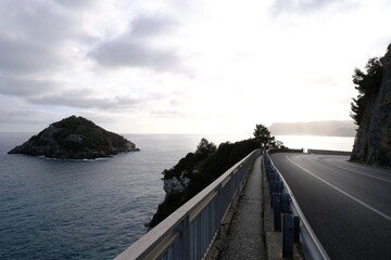A view of a coastal road against the light, along the Mediterranean Sea at Torre del Mare. Liguria, Italy - December 23, 2023.