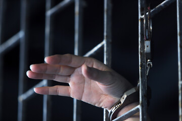 man behind jail bar with prisoner hands expresses feelings.