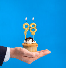 Hand holding a cupcake with the number 98 candle - Birthday on blue background
