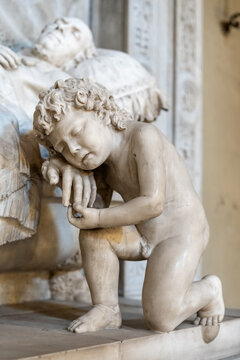 Close-up on marble statue of little naked boy kneeling in sorrow while holding the hand of a dead old man laying on a bed