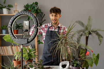 Young man influencer blogger blogging about houseplants, filming on a smartphone on a tripod.