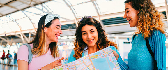 Three female traveler friends at the train station checking the city map