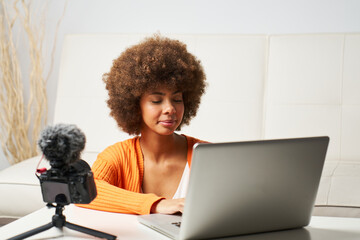 young latina woman with afro hair uses laptop to edit streaming video on social networks