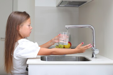 Little girl pouring water from fauset in kitchen, water filtration system