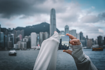 An Asian woman holds a mobile phone to take photos of modern architecture in Hong Kong