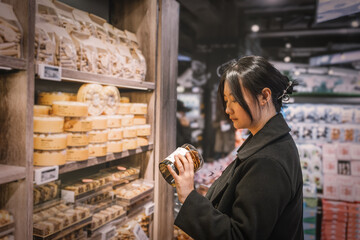 A young Asian girl is shopping in the food section of a supermarket, reading the nutritional labels...