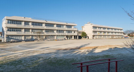 The exterior of a Japanese elementary school building and the empty dirt playing field in front of it on a cold January afternoon. 
