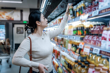 A young Asian girl is shopping in the beverage section of a supermarket, standing by the aisle with...