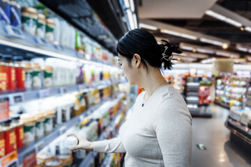 A young Asian girl is shopping in the beverage section of a supermarket, standing by the aisle with...