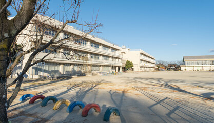 The exterior of a Japanese elementary school building and the empty dirt playing field in front of it on a cold January afternoon. 