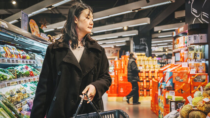 Young Asian girl buys fresh fruits in the fruit and vegetable section of the supermarket, adopts a...
