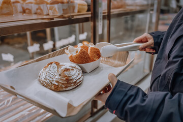 An Asian woman is selecting and buying bread at a dessert shop, and placing the bread on a wooden plate.