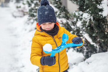 Fototapeta na wymiar Winter games outdoors. Small kid have fun making snowballs with toy plastic maker.