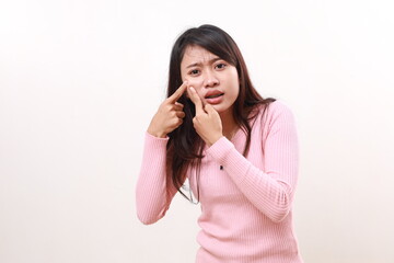 Fototapeta premium A young asian woman popping a pimple on her face while looking at the camera. Isolated on white