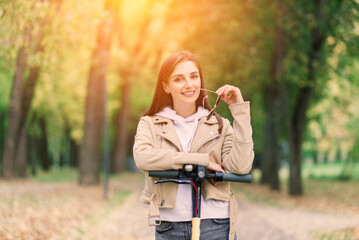 Young woman riding an electric scooter in an autumn park. Green transport, traffic jam problems.