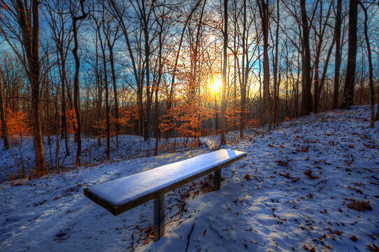 Empty Bench in the Snow. A snow covered bench provides a perfect view of the falling sun on this wintery afternoon along the hiking trail around Lake Tywappity Community Lake. 