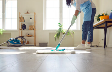 Housewife or professional cleaner mopping the floor at home. Crop young woman in an apron and...