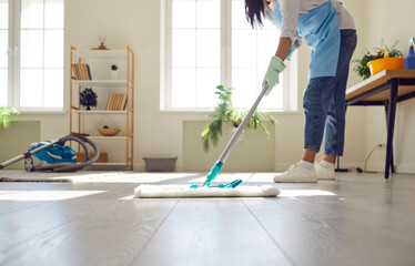 Housewife or professional cleaner mopping the floor at home. Crop young woman in an apron and gloves washing light gray wooden or laminate flooring in the living room. Housework, cleaning concept