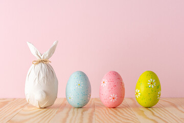 Easter egg wrapped in a paper in the shape of a bunny with colorful Easter eggs. Minimal Easter background. Spring holidays concept.