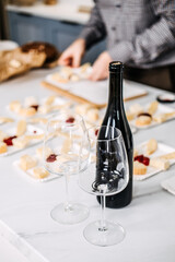 Preparing Appetizers with Wine for a Gathering. Unfocused hands arranging cheese and bread appetizers on a marble counter, with an empty wine bottle and glasses in the foreground.