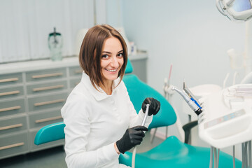 Young female dentist holds instruments in her hands in the interior of a modern dental clinic. The concept of professional activity, dental instruments and services.