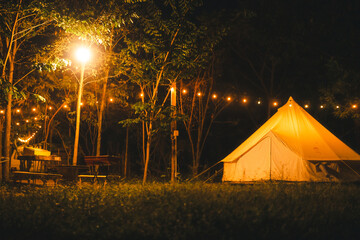 Night and warm light exposure of an illuminated bell tent surrounded by trees and a small camp fire...