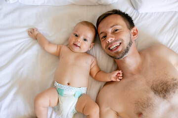 Portrait of a father and a cute carefree newborn child lying on a bed, top view