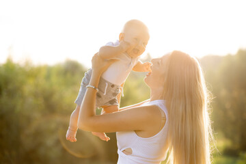 young happy and beautiful woman holding her adorable little baby boy outdoors on sunset