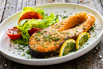 Fried salmon steak and fresh vegetable salad served on wooden table
