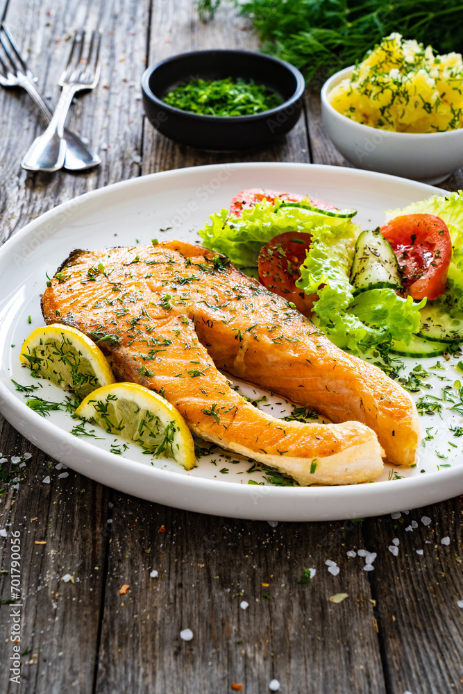 Wall mural Fried salmon steak and fresh vegetable salad served on wooden table
