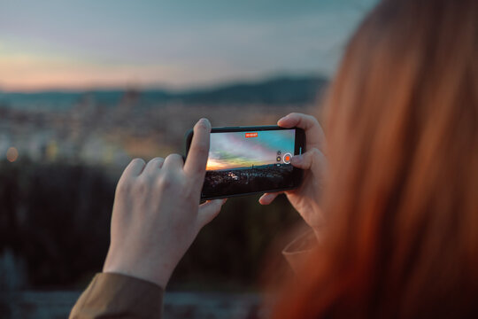 back view of female take a photo of golden sunset over Palazzo Vecchio and Cathedral of Santa Maria del Fiore (Duomo), Florence, Italy. High quality photo